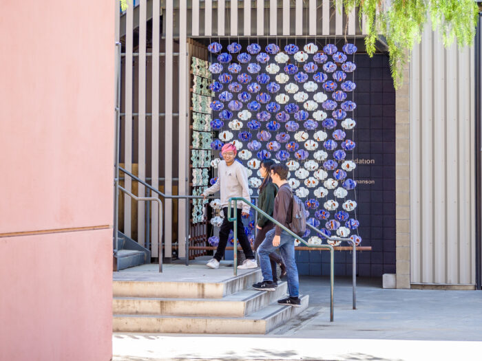 Three students walking in front of a purple patchwork ceramic sculpture.