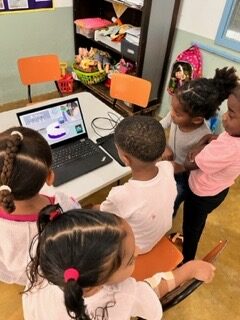 students gathered around a computer with the cake game on it.