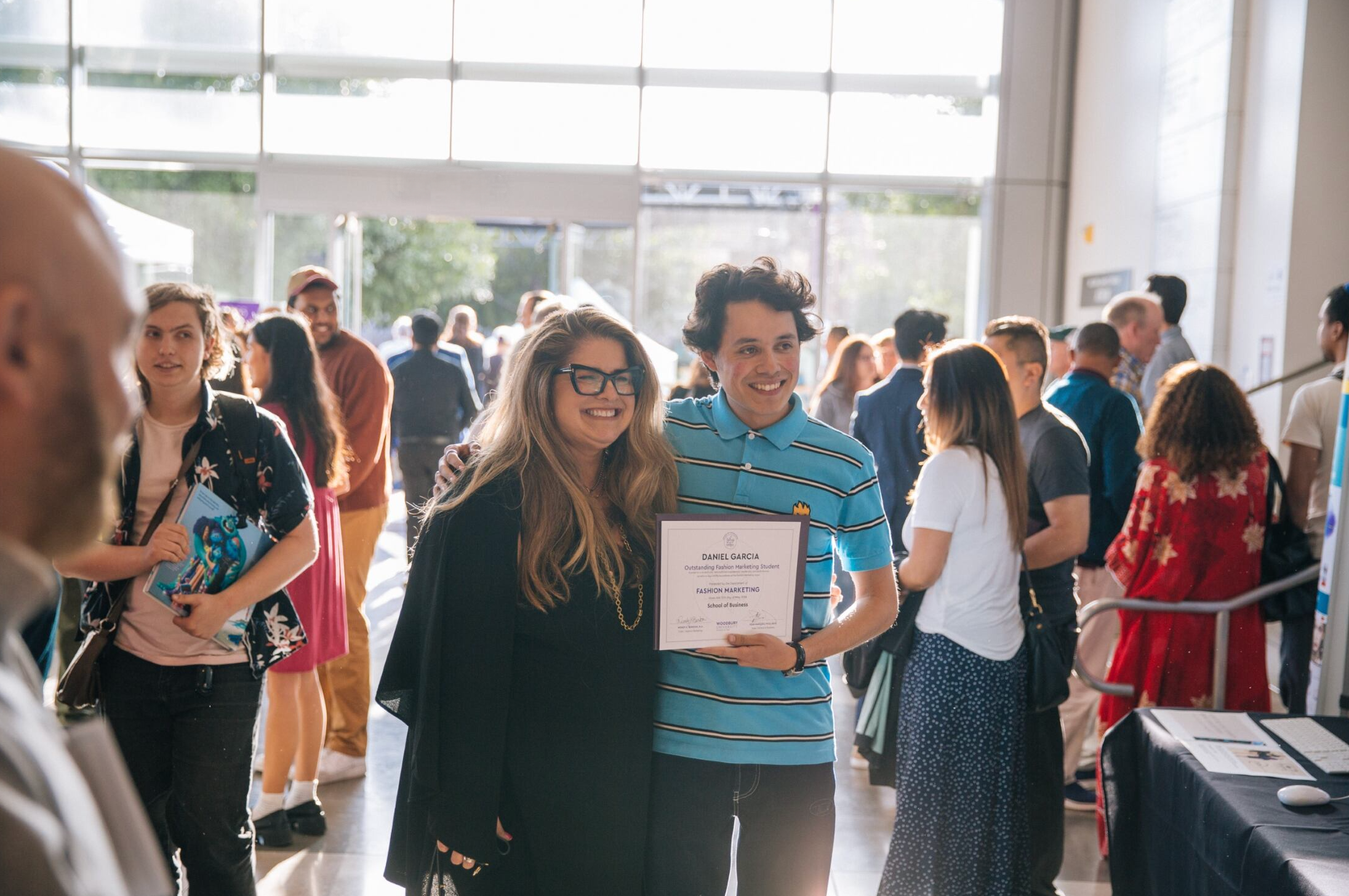 Professor and Student holding an award smile in a crowd of people.